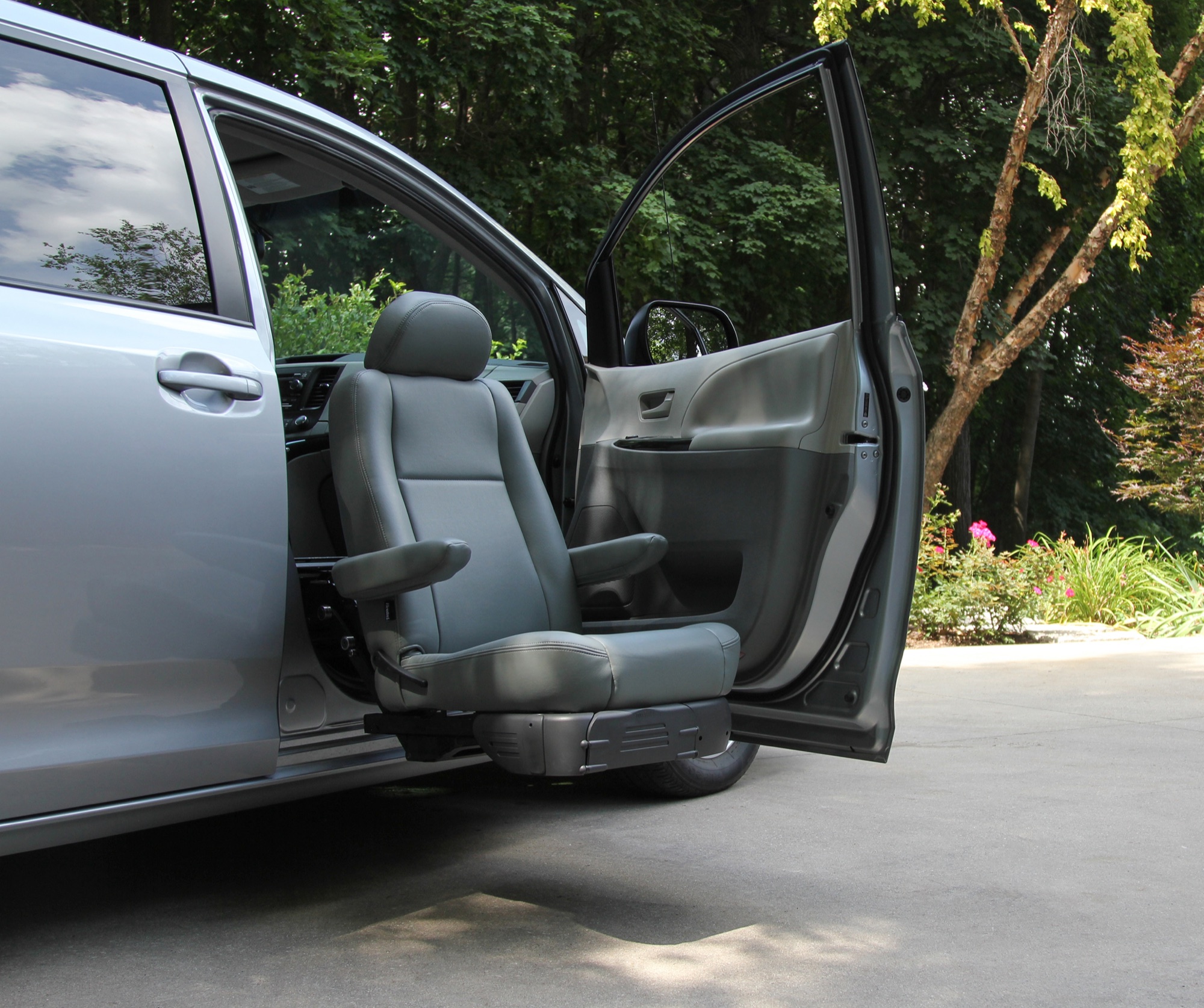 A Turny Evo transfer seat fully extended from the open front passenger door of a silver Toyota Sienna.